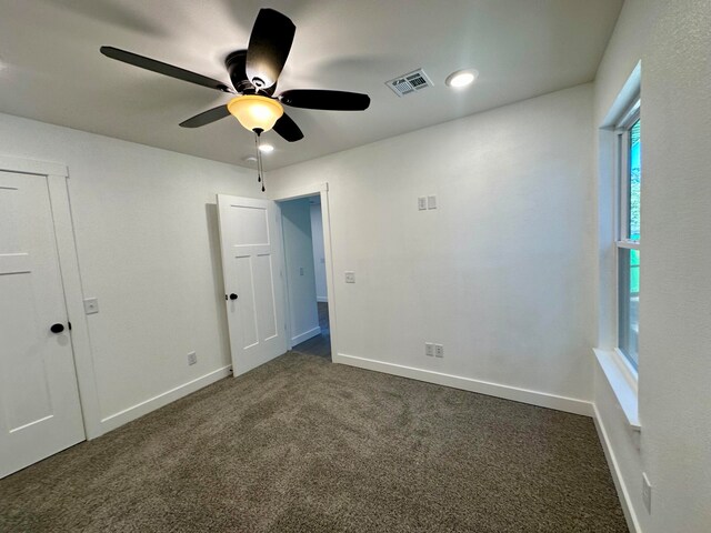 empty room with ceiling fan and dark colored carpet