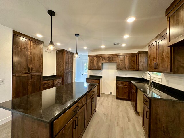 kitchen featuring a kitchen island, dark stone countertops, sink, pendant lighting, and light hardwood / wood-style floors