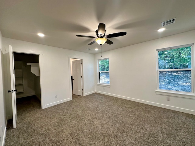 unfurnished bedroom featuring dark carpet, a spacious closet, and ceiling fan