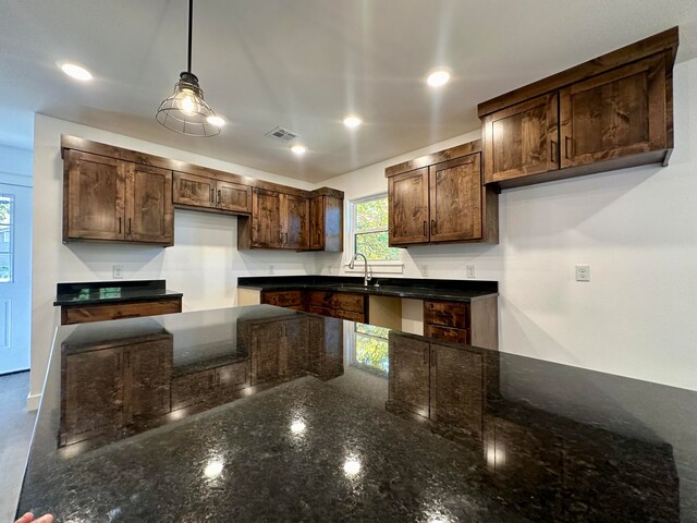 kitchen with pendant lighting, sink, dark brown cabinets, and dark stone counters