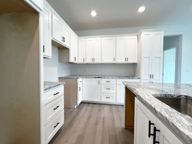 kitchen with white cabinets, light stone countertops, and light wood-type flooring