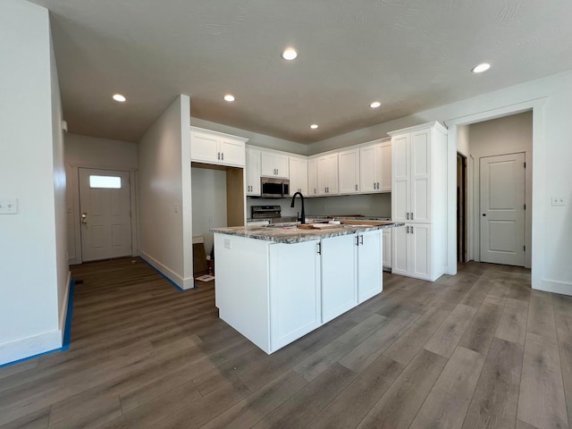 kitchen with hardwood / wood-style floors, black range with electric stovetop, a center island with sink, white cabinetry, and dark stone counters