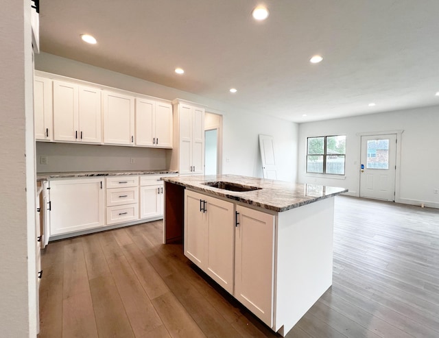 kitchen featuring a center island with sink, light stone countertops, light wood-type flooring, and white cabinets