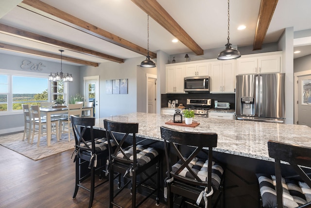 kitchen featuring stainless steel appliances, pendant lighting, dark hardwood / wood-style floors, white cabinetry, and a breakfast bar area