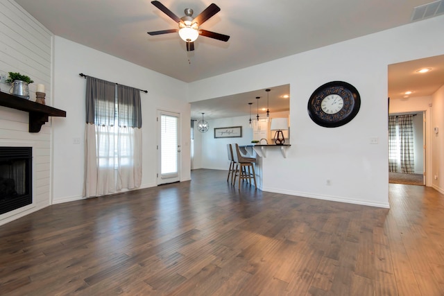 unfurnished living room featuring dark wood-type flooring, a fireplace, and ceiling fan with notable chandelier