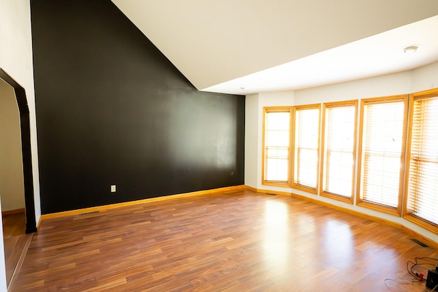 spare room with a healthy amount of sunlight, lofted ceiling, and hardwood / wood-style floors