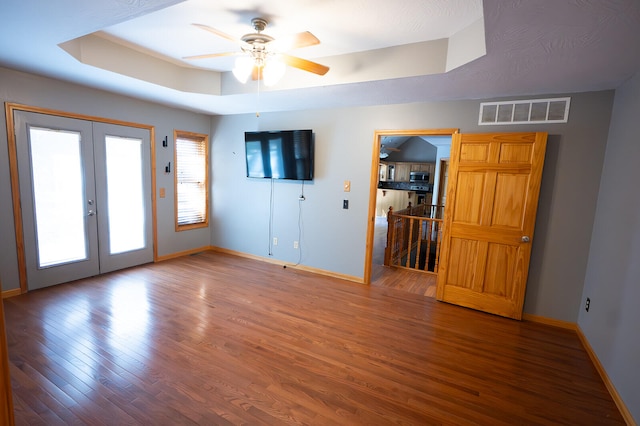 spare room featuring french doors, hardwood / wood-style flooring, a tray ceiling, and ceiling fan