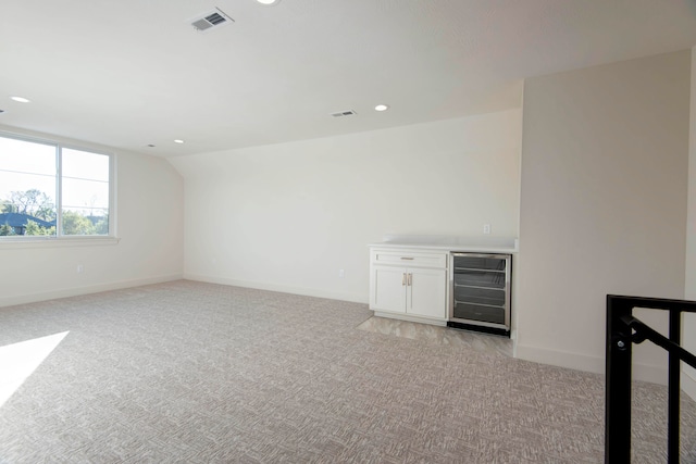 bar with white cabinetry, wine cooler, and light carpet