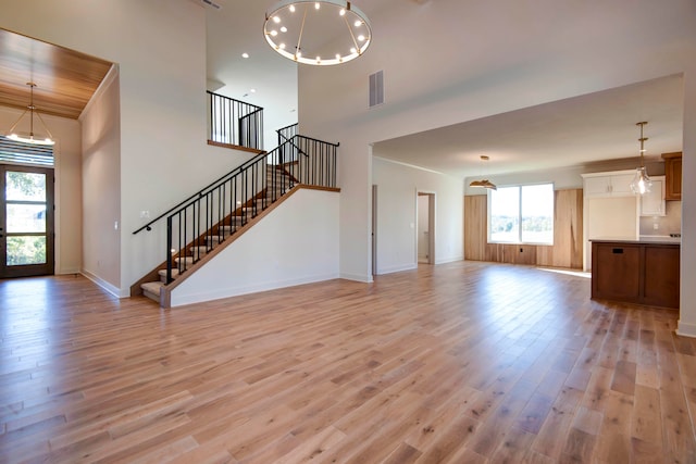 unfurnished living room featuring an inviting chandelier, a high ceiling, and light wood-type flooring