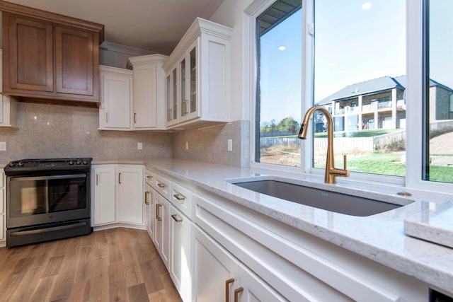 kitchen with black electric range oven, white cabinets, light stone countertops, light wood-type flooring, and sink