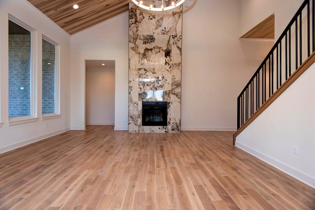 unfurnished living room with light hardwood / wood-style floors, wood ceiling, a premium fireplace, and high vaulted ceiling