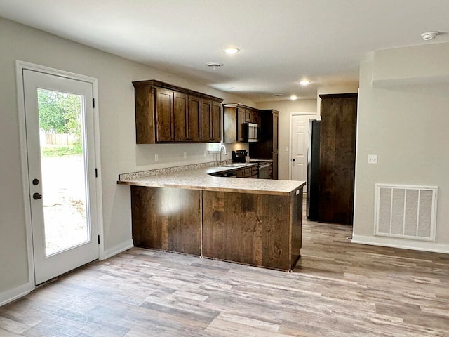 kitchen featuring appliances with stainless steel finishes, kitchen peninsula, dark brown cabinetry, and light wood-type flooring