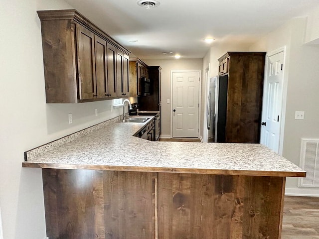 kitchen with kitchen peninsula, hardwood / wood-style floors, stainless steel appliances, and dark brown cabinets