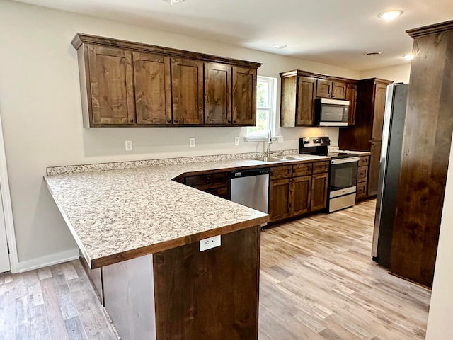 kitchen featuring appliances with stainless steel finishes, sink, kitchen peninsula, light hardwood / wood-style floors, and dark brown cabinetry