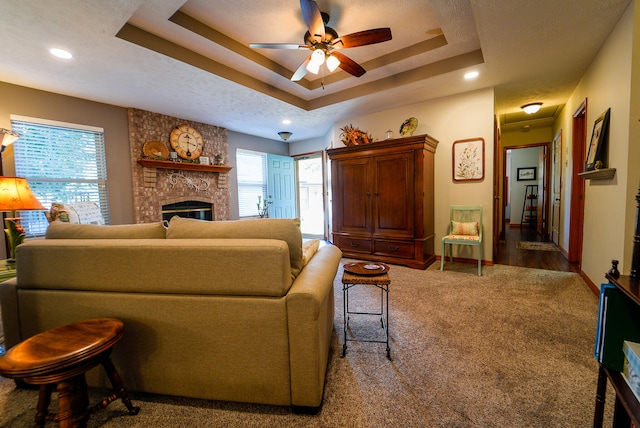 carpeted living room with ceiling fan, a raised ceiling, a textured ceiling, and a large fireplace