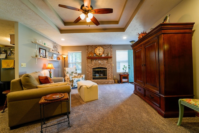 living room featuring ceiling fan, a fireplace, a textured ceiling, and a raised ceiling