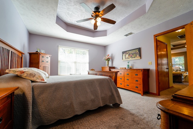 carpeted bedroom with ceiling fan, a raised ceiling, and a textured ceiling