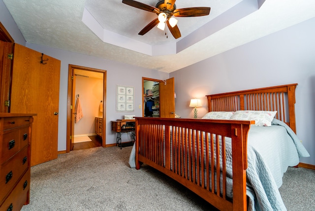 carpeted bedroom with a textured ceiling, ensuite bathroom, a raised ceiling, and ceiling fan