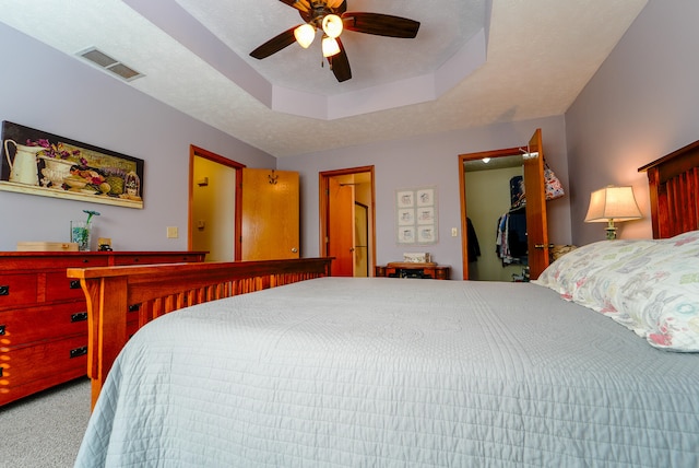 bedroom featuring a spacious closet, carpet, ceiling fan, and a raised ceiling