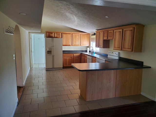 kitchen with lofted ceiling, kitchen peninsula, light tile patterned floors, a textured ceiling, and white appliances