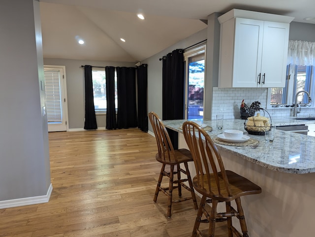 kitchen featuring a breakfast bar area, backsplash, light stone countertops, light hardwood / wood-style floors, and white cabinets