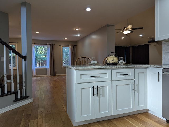 kitchen with light hardwood / wood-style floors, light stone countertops, kitchen peninsula, and white cabinets