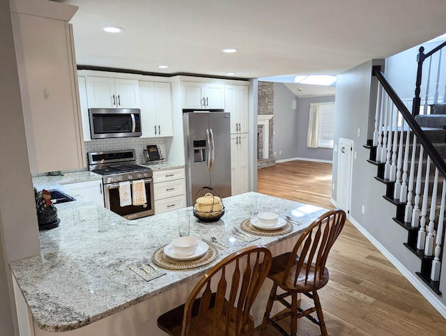 kitchen with a breakfast bar, light stone counters, light hardwood / wood-style flooring, kitchen peninsula, and stainless steel appliances