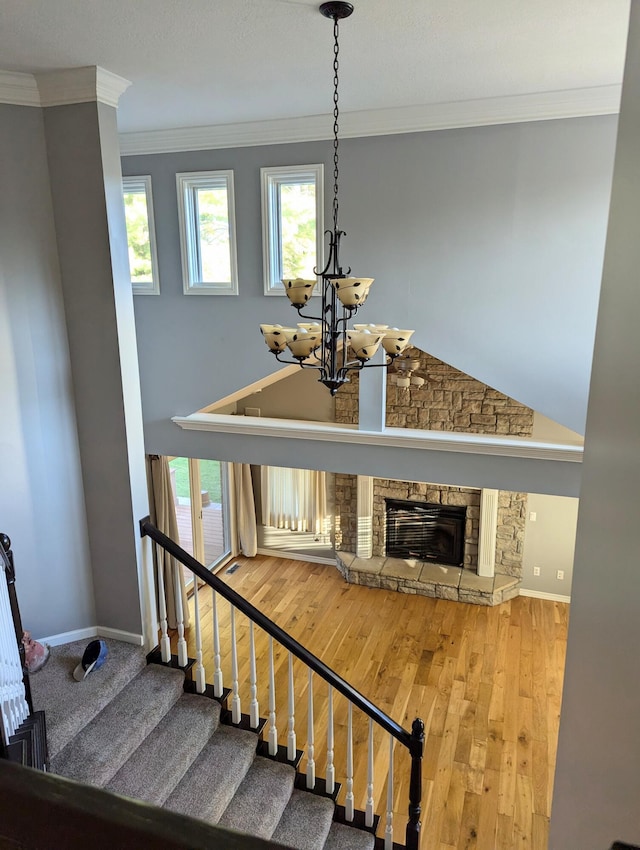 stairs featuring hardwood / wood-style flooring, crown molding, a stone fireplace, and an inviting chandelier