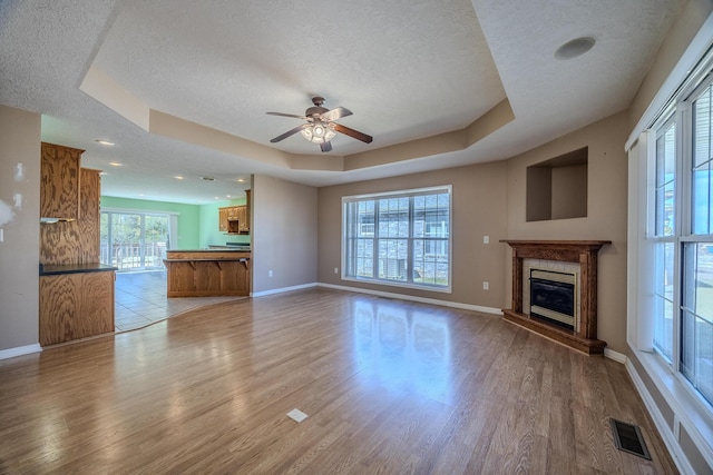 unfurnished living room with a tray ceiling, a textured ceiling, visible vents, and light wood-style floors