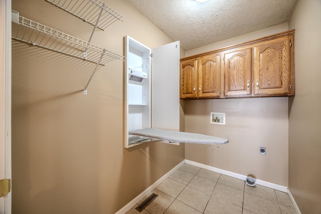 laundry room featuring electric dryer hookup, hookup for a washing machine, light tile patterned floors, a textured ceiling, and cabinets