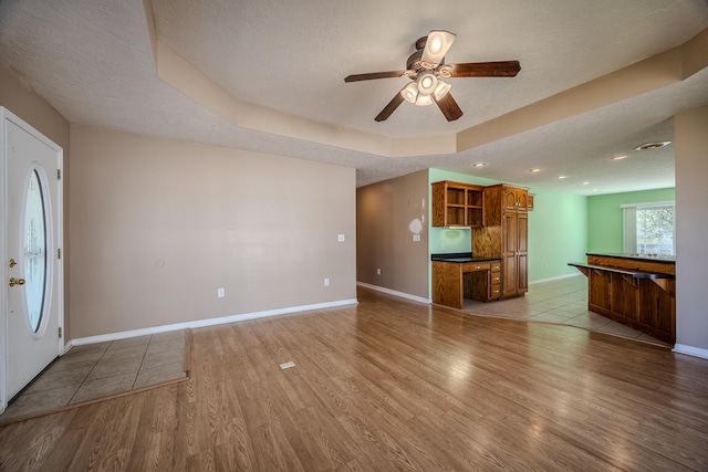 unfurnished living room featuring light hardwood / wood-style flooring, a textured ceiling, a tray ceiling, and ceiling fan