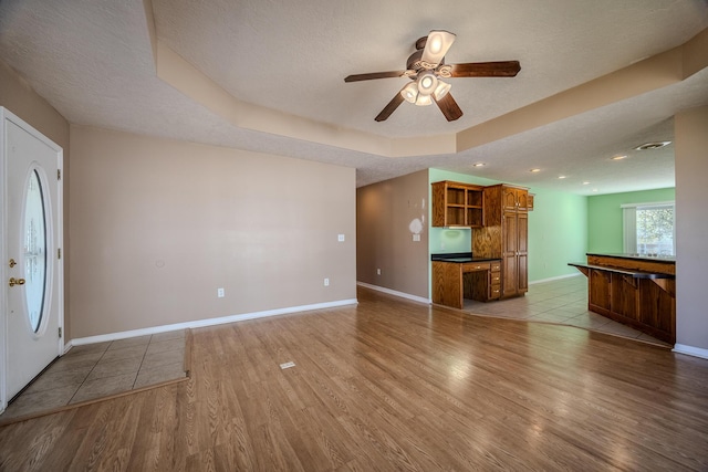 unfurnished living room featuring a tray ceiling, wood finished floors, a ceiling fan, baseboards, and a textured ceiling