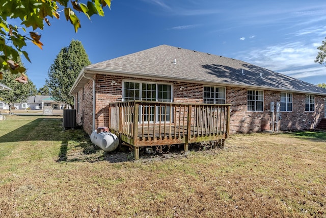 rear view of house with roof with shingles, central AC unit, a wooden deck, brick siding, and a yard