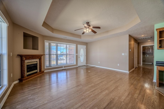 unfurnished living room featuring a tray ceiling, baseboards, a premium fireplace, wood finished floors, and ceiling fan