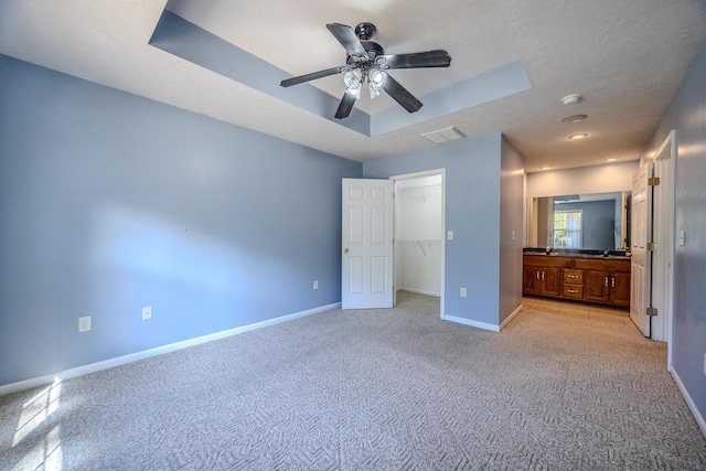 unfurnished bedroom with a walk in closet, baseboards, light carpet, and a tray ceiling
