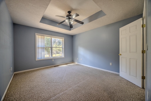 carpeted empty room featuring ceiling fan, a raised ceiling, and a textured ceiling