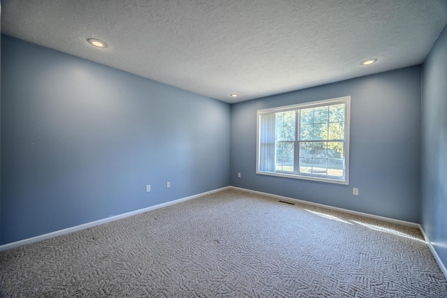 carpeted empty room featuring a textured ceiling, visible vents, and baseboards