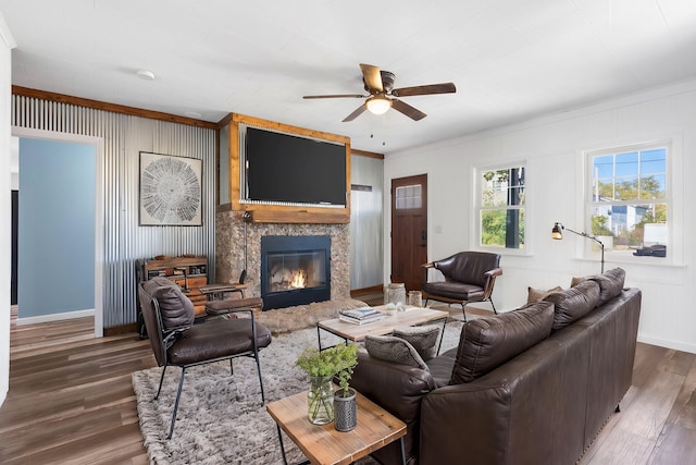 living room with dark wood-type flooring, crown molding, a premium fireplace, and ceiling fan