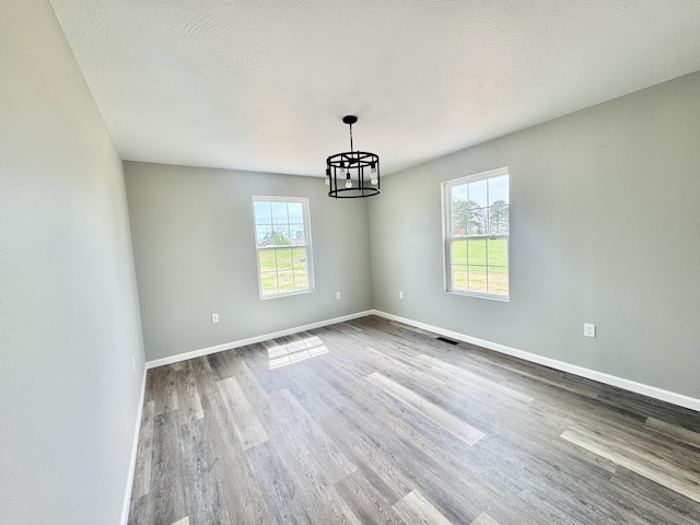 unfurnished room featuring wood finished floors, baseboards, a chandelier, and visible vents