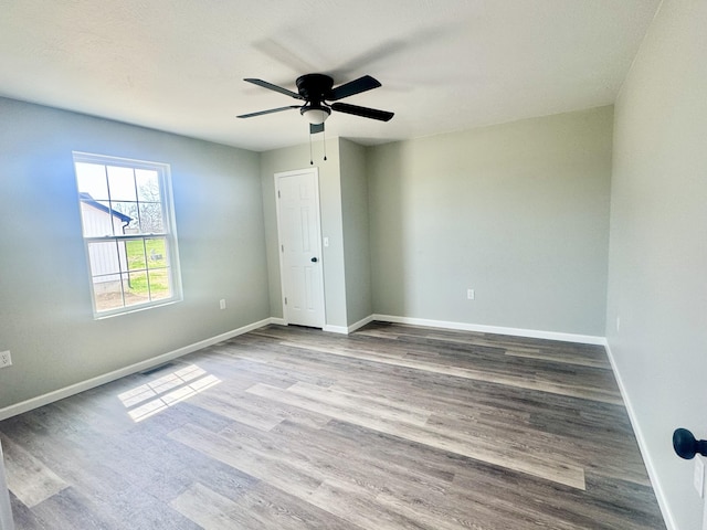 empty room with baseboards, visible vents, a ceiling fan, and wood finished floors