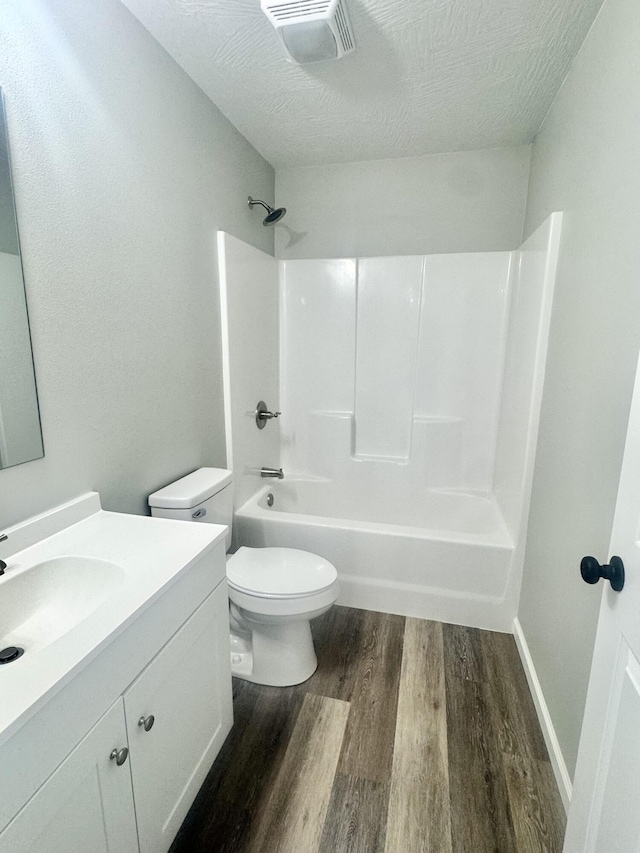 bathroom with a textured ceiling, visible vents, toilet, wood finished floors, and vanity
