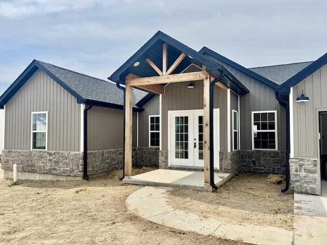 view of front of home featuring stone siding, french doors, and roof with shingles