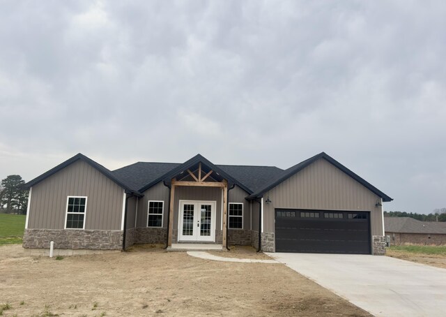 view of front of property with stone siding, an attached garage, concrete driveway, board and batten siding, and french doors