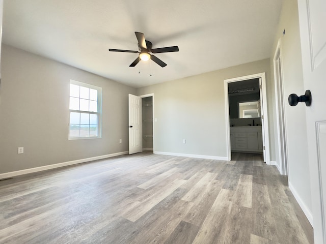 unfurnished bedroom featuring light wood finished floors, baseboards, ceiling fan, and ensuite bathroom