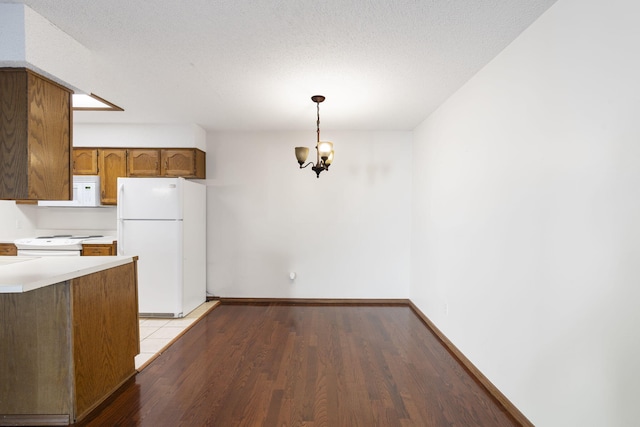 kitchen featuring white appliances, decorative light fixtures, a textured ceiling, a notable chandelier, and light hardwood / wood-style floors