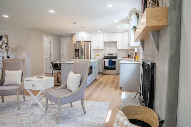 kitchen featuring appliances with stainless steel finishes, sink, light wood-type flooring, hanging light fixtures, and white cabinetry