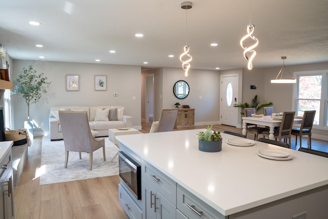 kitchen with stainless steel microwave, light wood-type flooring, gray cabinetry, decorative light fixtures, and a center island