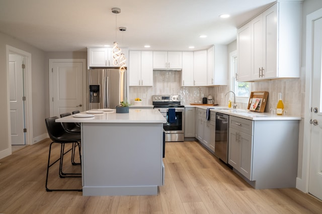 kitchen featuring appliances with stainless steel finishes, light wood-type flooring, a kitchen island, decorative light fixtures, and white cabinets