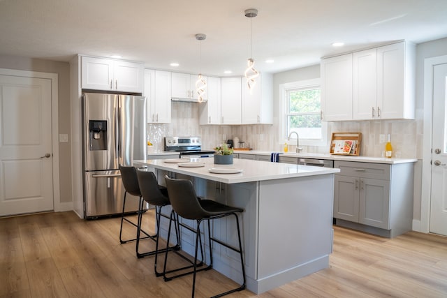 kitchen featuring a kitchen island, light hardwood / wood-style flooring, stainless steel appliances, pendant lighting, and white cabinetry