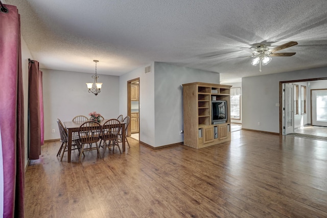 dining area with ceiling fan with notable chandelier, a healthy amount of sunlight, a textured ceiling, and dark hardwood / wood-style floors